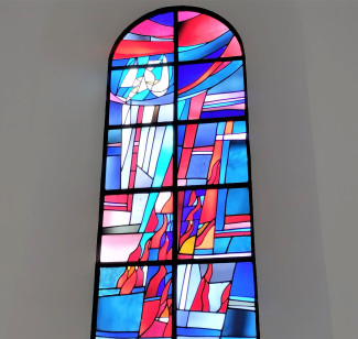 Das rechte Fenster im Chorraum der Dreifaltigkeitskirche symbolisiert Pfingsten durch rote flammenartige Glasstücke, sowie eine weiße Taube vor verschiedenen Blautönen im Hintergrund.