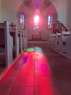 Die Abendsonne leuchtet durch die bunten Fenster der Kirche und taucht den ganzen Kirchenraum in bunte Farben.