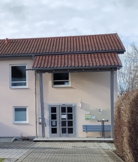 Der Eingang des Gemeindehauses mit der grauen Glastüre unter dem großen Vordach.