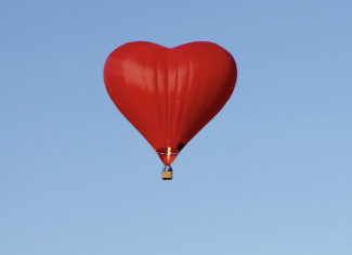 Ein roter Heißluftballon in herzform vor blauem Himmel